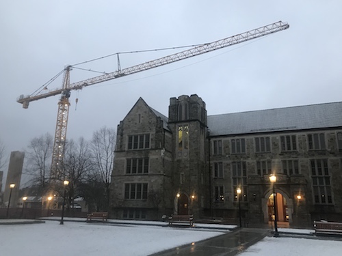Fulton Hall at twilight in the snow with a construction crane looming in the background