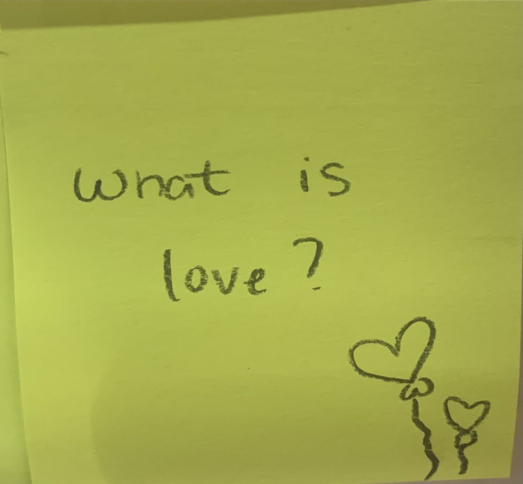 What is love? (Small drawing of heart baloons at the bottom of the stickynote)