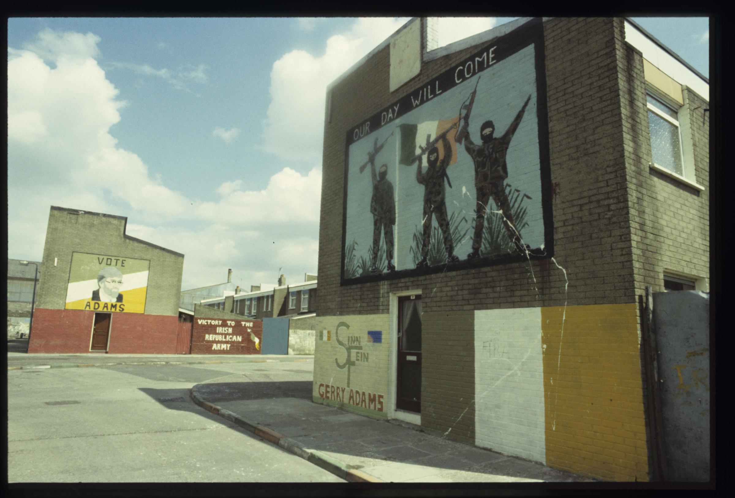 Republican murals on buildings featuring a portrait of Gerry Adams and three men armed with rifles