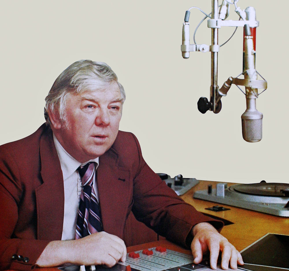 Photograph of Ciarán Mac Mathúna, seated at a desk in front of a microphone