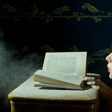 Photograph of a woman blowing dust off of a book