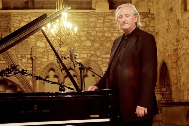 Mícheál Ó Súilleabháin standing next to a grand piano