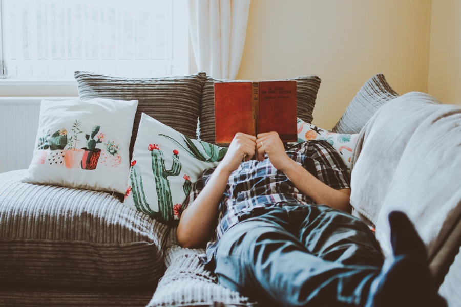 man reclining on couch reading with book cover concealing his face