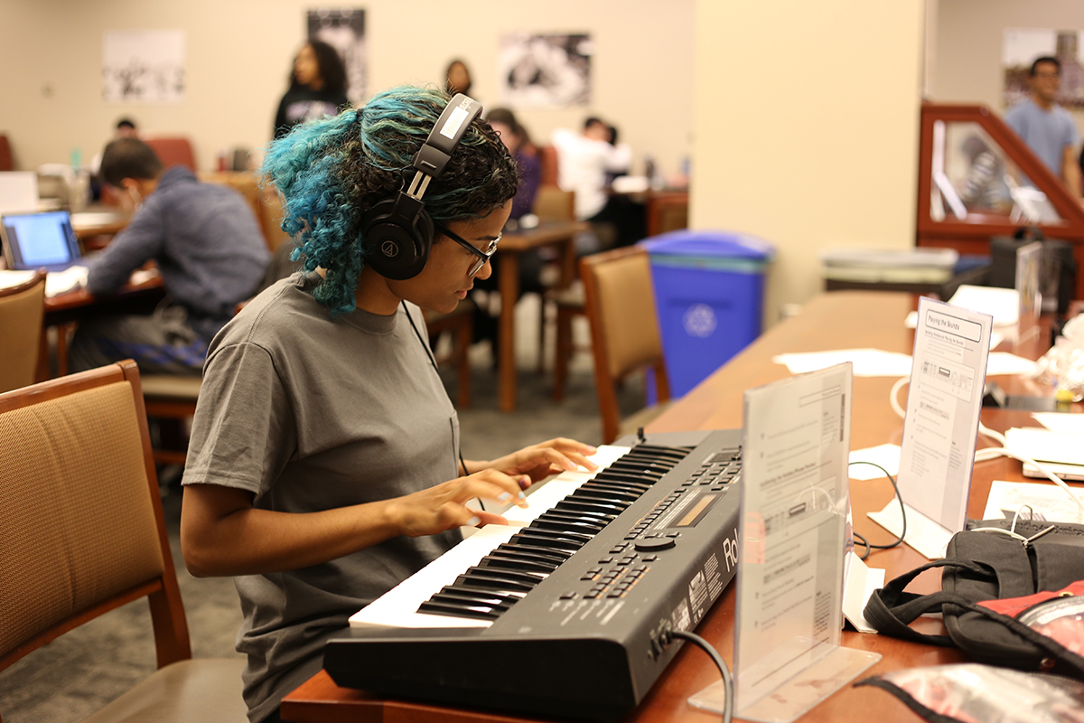 A student sits at a desk playing a keyboard.