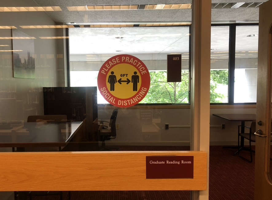 Photo of O'Neill Library Graduate Reading Room with round red and yellow sign, saying "Please practice social distancing, 6 ft."