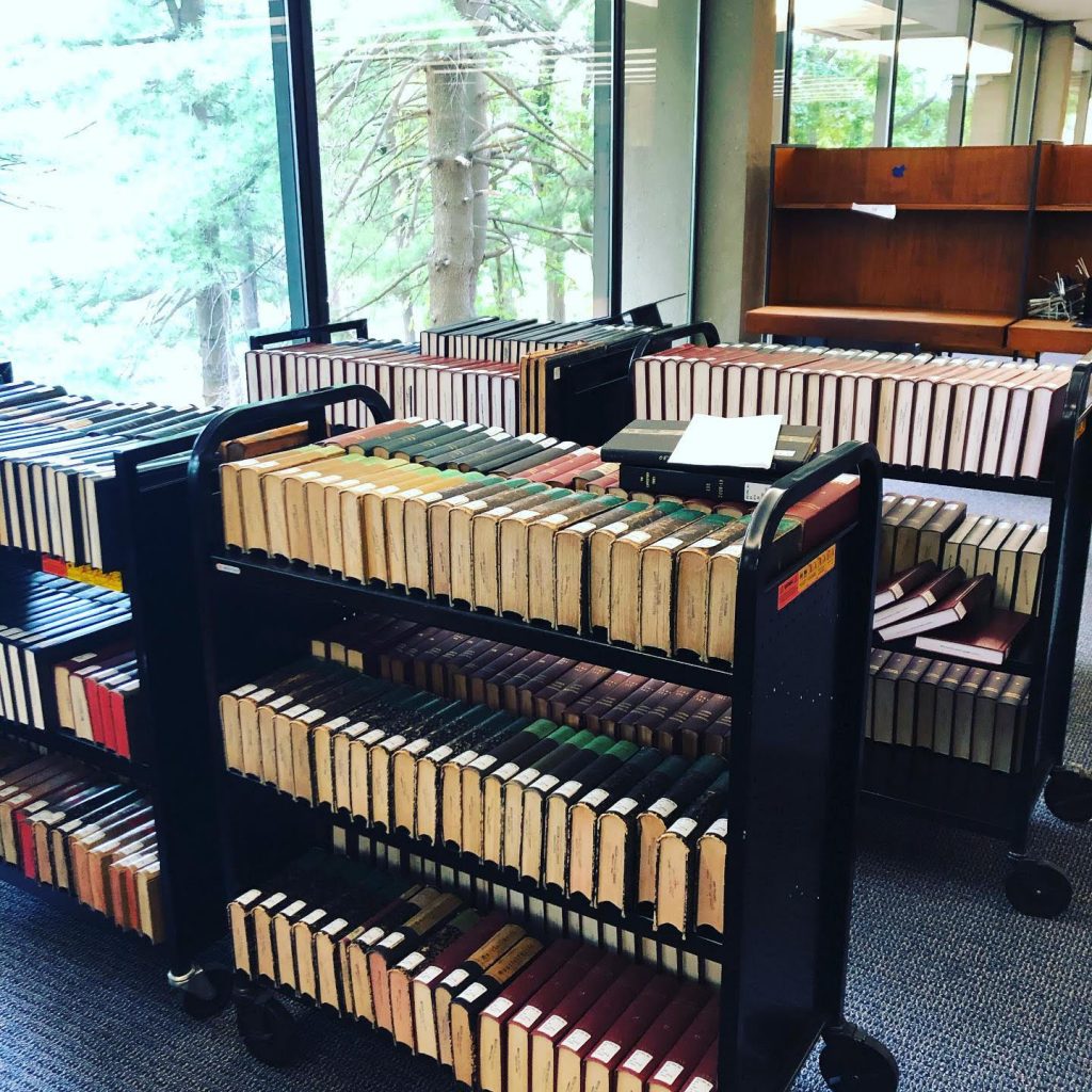 Six book carts full of periodical volumes await processing in TML, next to a window with a view of trees.