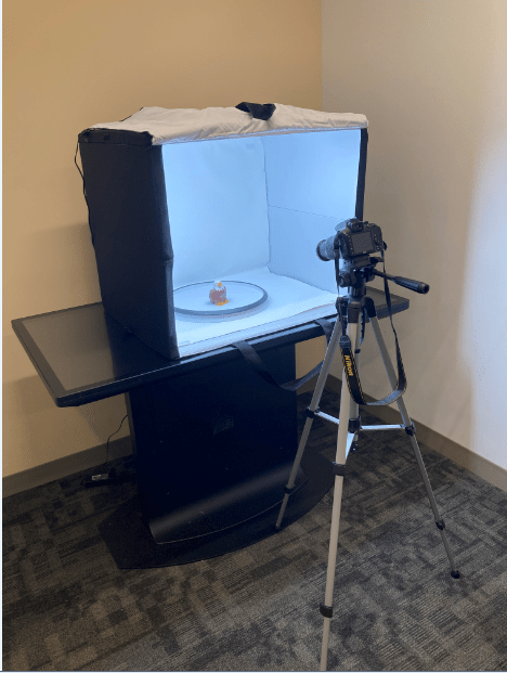 3d digital modeling station in the Digital Studio: a camera positioned on a tripod in front of a light-flooded box containing a small BC Eagle toy being imaged.