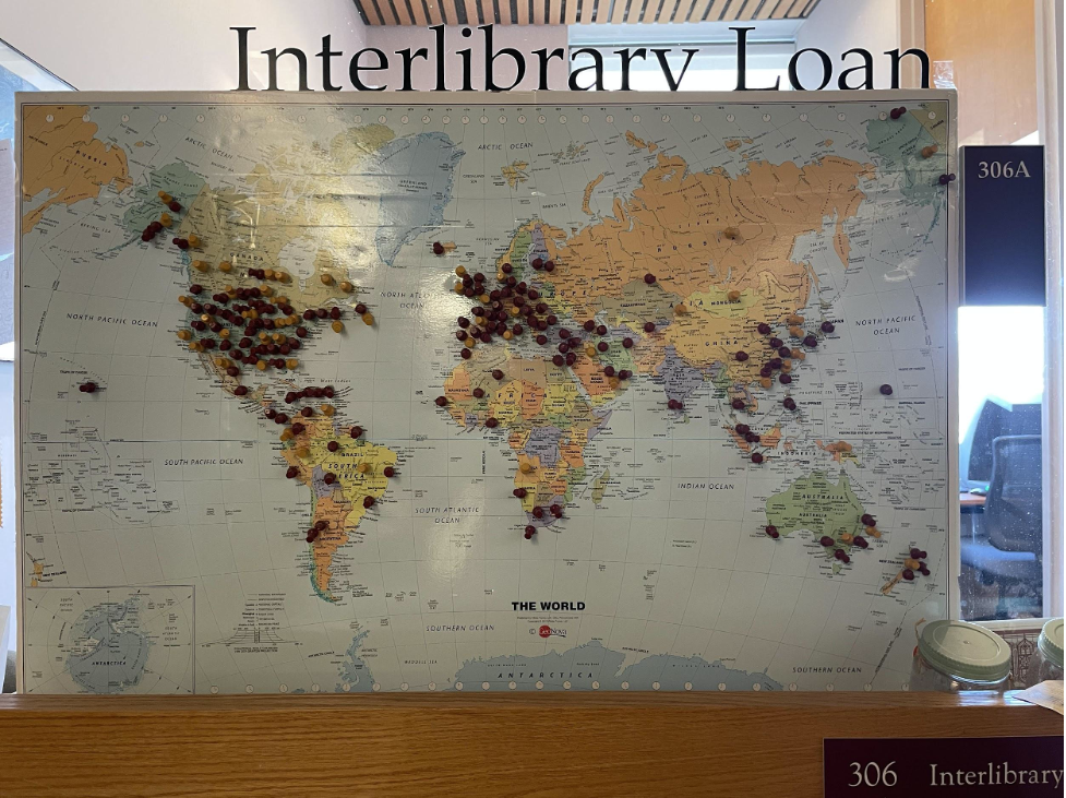 Photo of a world map in the window of the ILL office in O'Neill Library, with yellow and red pushpins all over the world denoting location of libraries the office has borrowed from or loaned to in the last few years.
