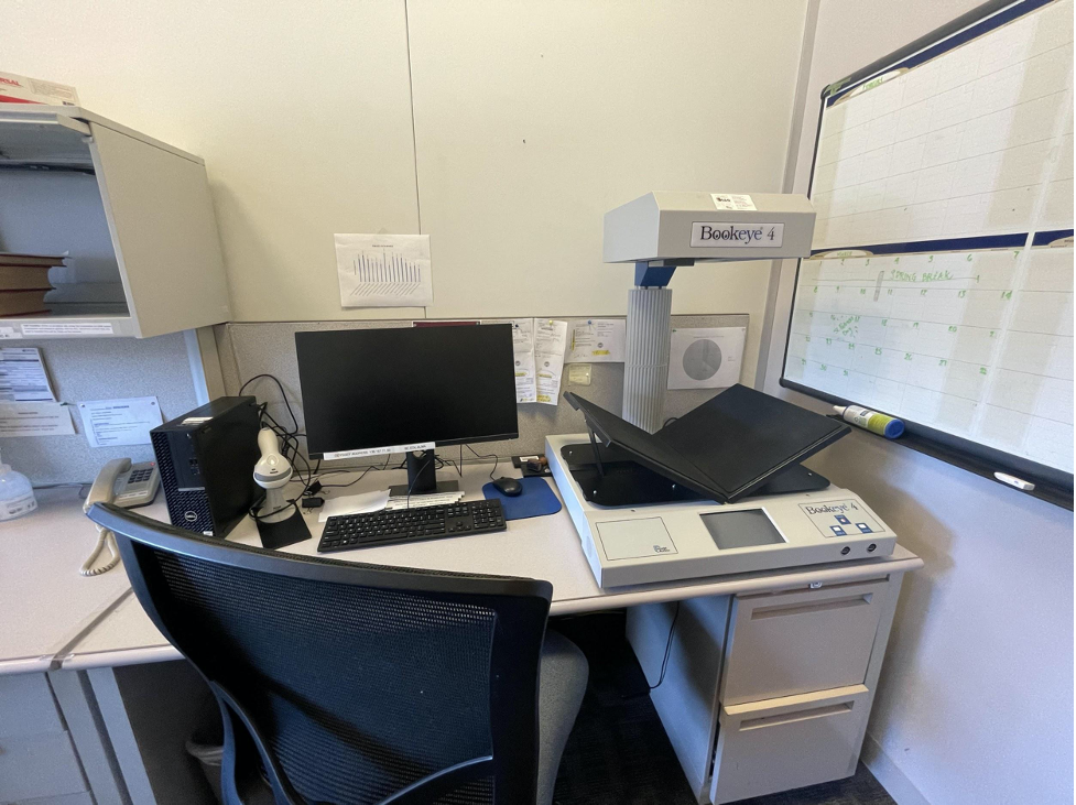 Photo of a desk with a computer and overhead scanner with an angled book tray in the ILL office.