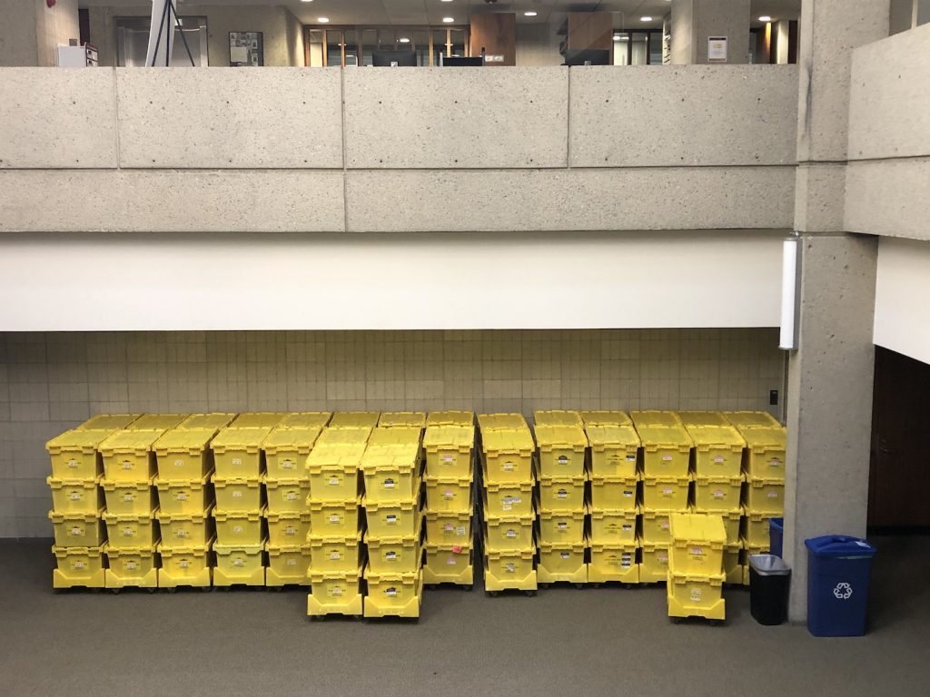 30 stacks of crates, each 4 crates high, stand against a ground-floor wall in an open area.