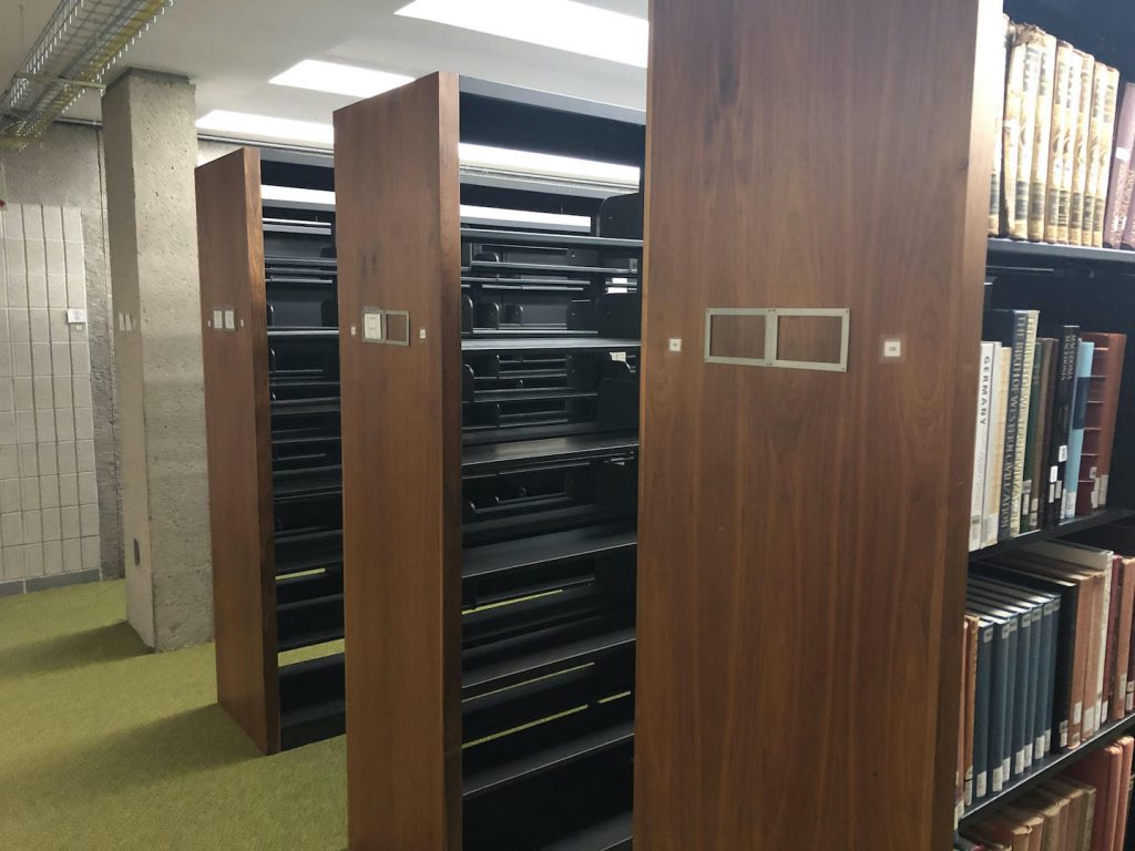 Two empty dark metal shelving rows with attractive wooden end-caps. A row full of books is on the right in the foreground.