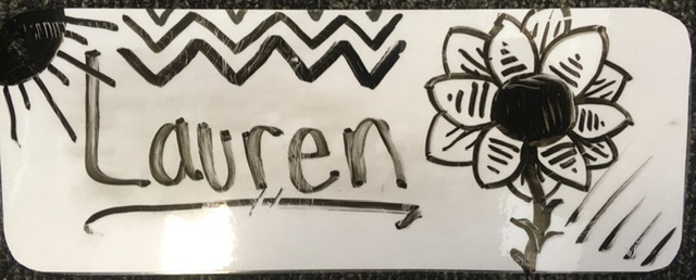 The name "Lauren" in black dry-erase ink on a laminated card, decorated with a sun, some diagonal lines, and a sunflower.