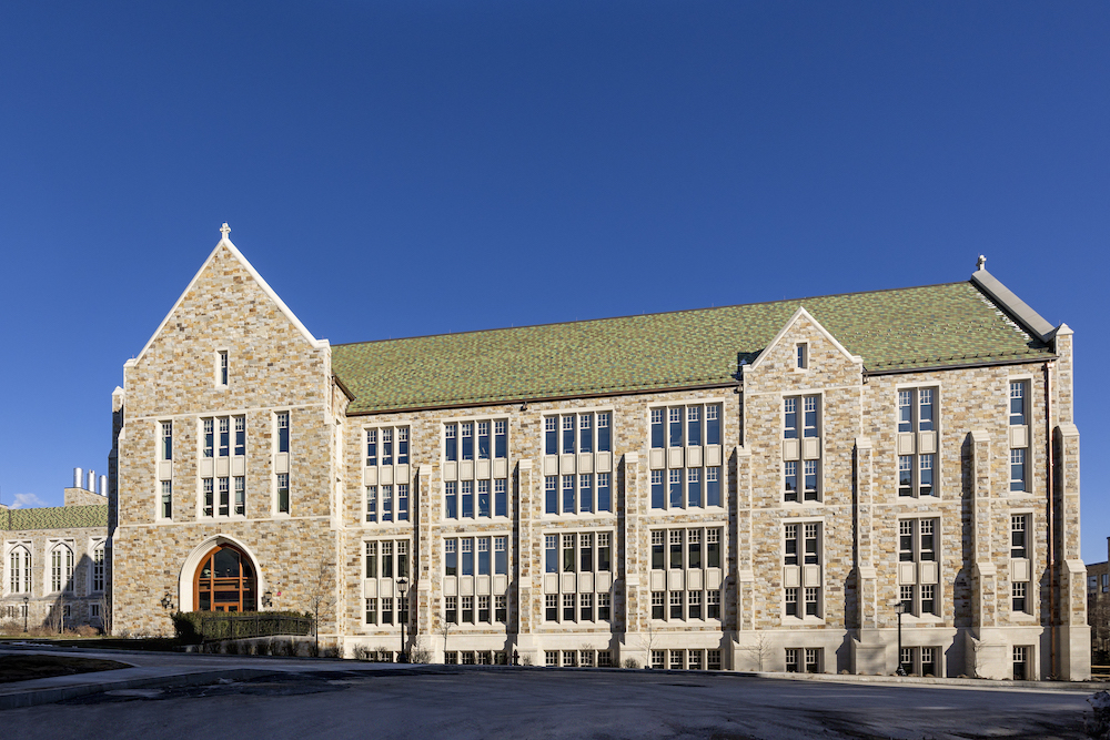 Exterior view of a 4 story neogothic building with a green roof, under a stunning blue sky.