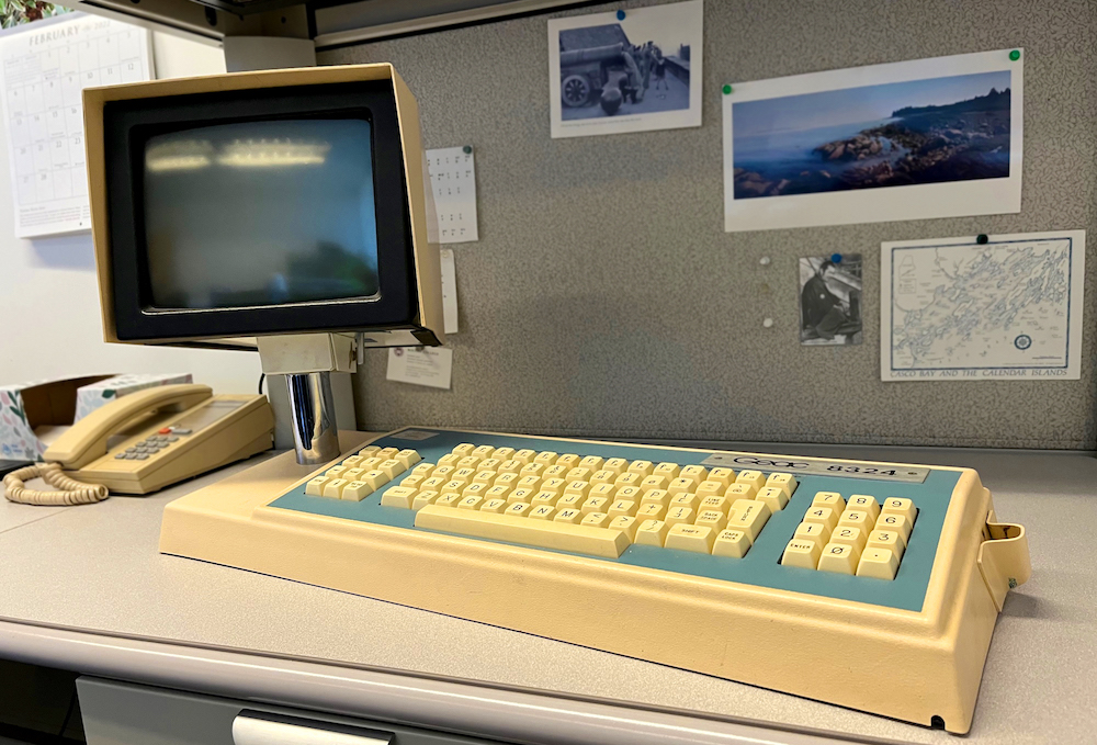 An old computer keyboard with an attached screen on a post, labeled "Geac 8324"
