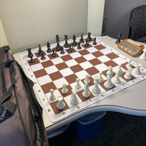 Classic chess set with brown and black pieces on a roll-up brown and white board next to a digital timer.