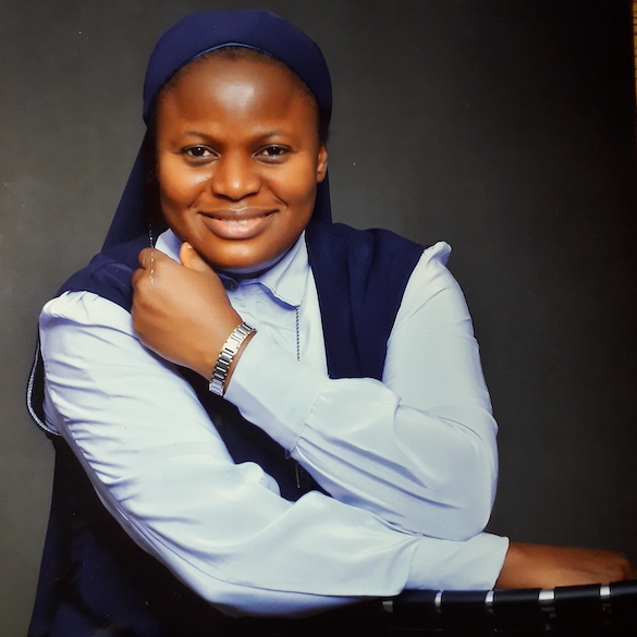 Photo of person in light blue blouse and navy blue vest and headcovering.