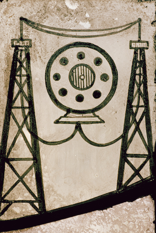 Stained glass panel in sepia-tone and black lines, with a round object surrounded by two radio towers