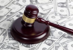 A wooden courtroom gavel rests on its round wooden base on a surface covered with $100 bills.