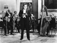 John McCormack performing in the film Wings of the Morning (1937), shown holding one of his lyric books.